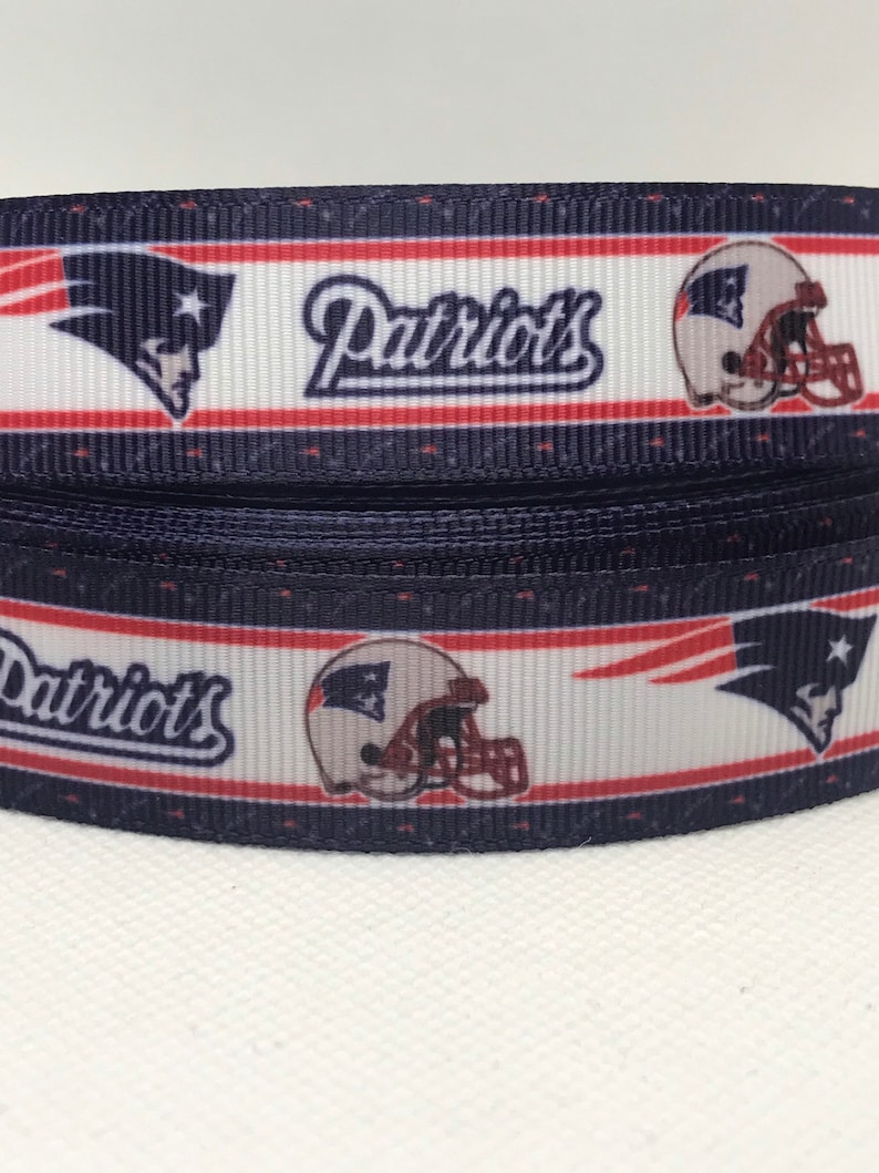 May include: A white, red, and blue ribbon with the words "Patriots" and a football helmet graphic.