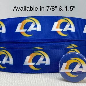 May include: Blue ribbon with repeating white and yellow "LA" logo pattern. A matching button is also visible. Text at the top reads "Available in 7/8" & 1.5""