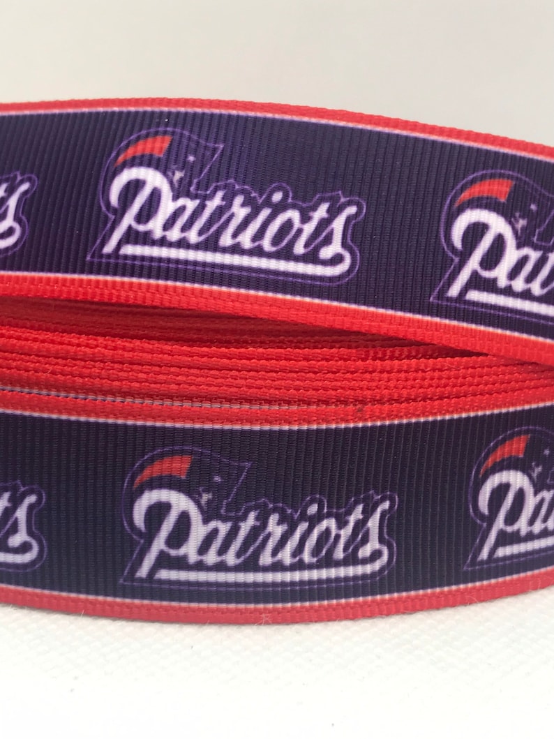 May include: Red, white, and blue ribbon with the word "Patriots" printed on it. The ribbon is made of a soft, woven fabric.