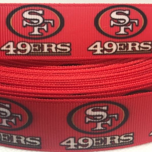 以下が含まれることがあります： サンフランシスコ・フォーティナイナーズのロゴと「49ers」という文字が繰り返された赤と金のリボンです。