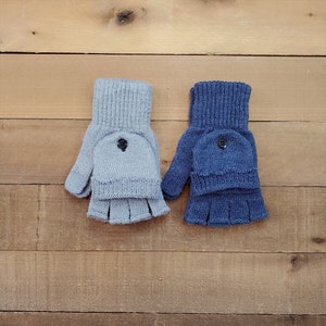 May include: Two pairs of fingerless gloves, one in light blue and one in dark blue. Both pairs have a button on the back of the hand.