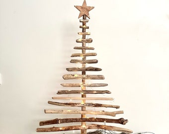 May include: A rustic wooden Christmas tree made from driftwood branches, decorated with string lights and a wooden star on top. The tree is standing on a wooden base and is surrounded by dried lavender, pine cones, and red berries.