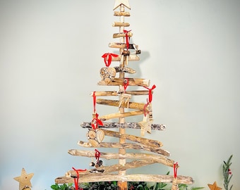 May include: A rustic wooden Christmas tree with a star topper and red ribbon accents. The tree is constructed from natural wood pieces and adorned with small wooden ornaments. Additional wooden star and cone-shaped trees are also present.