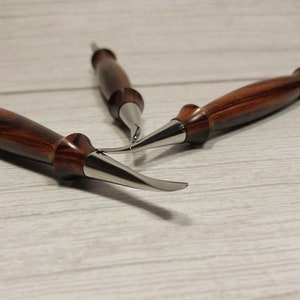 May include: Three wood-handled carving tools with metal blades. The tools have a dark brown wood handle with a reddish-brown grain pattern. The blades are silver and have a curved shape.