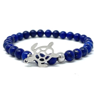 Può includere: Un braccialetto di perline di lapislazzuli blu con un ciondolo a forma di tartaruga d'argento.