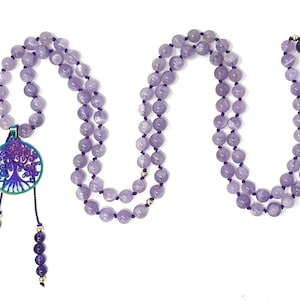 May include: A purple amethyst mala necklace with a tree of life pendant. The pendant is iridescent and has a gold-coloured accent. The necklace is made of 108 beads and has a tassel.