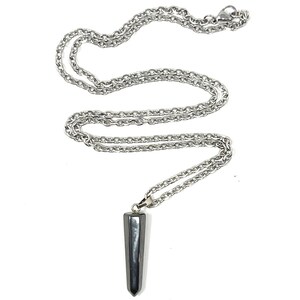 Op de afbeelding: Een zilverkleurige metalen ketting met een gladde, donkergrijze, langwerpige zeshoekige hanger. De hanger heeft een puntige onderkant en hangt aan een eenvoudig metalen oogje dat is bevestigd aan de gepolijste schakelketting met een karabijnsluiting.