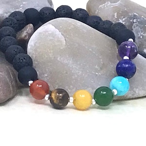 Könnte beinhalten: Ein schwarzes Lava-Armband mit sieben Chakra-Perlen. Die Perlen sind Amethyst, Lapislazuli, Türkis, grüner Aventurin, Citrin, Tigerauge und Karneol.