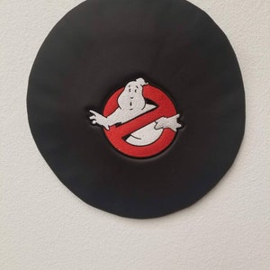 以下が含まれることがあります： 黒革のベレー帽に、赤と白の刺繍でゴーストバスターズのロゴが施されています。ロゴには、禁止記号の中に幽霊が描かれています。