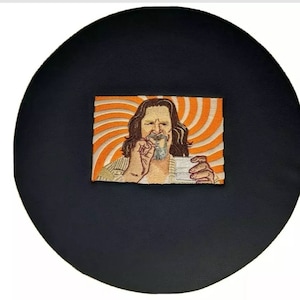 May include: Embroidered patch featuring a portrait of a man with long hair and a beard, holding a cup. The background has an orange and white spiral design. The patch is set on a black circular background.