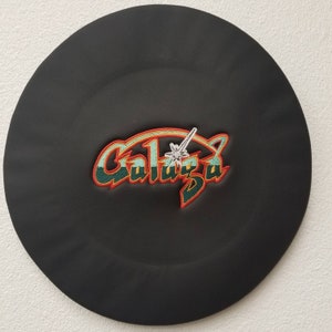 May include: Black, round hat with the embroidered word "Galaza" in a retro font. The text is in teal and red with a white star and sword design. The hat has a textured appearance.