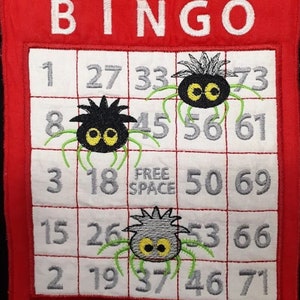 Può includere: Un cartoncino da bingo bianco con un bordo rosso e la parola "BINGO" in alto. Il cartoncino ha i numeri da 1 a 75 e tre ragni neri e grigi con le zampe verdi. Il quadrato centrale dice "Spazio libero".