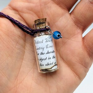 Puede incluir: Una pequeña botella de vidrio con un tapón de corcho y un collar de cordón morado. La botella contiene un trozo de papel enrollado con el texto "Detect Magic lasting Time for the duration object in the thin sheet of". Un amuleto azul de ojo turco está unido al collar.