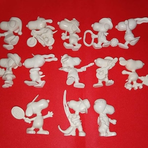 May include: A collection of 14 white plastic figurines of a cartoon dog, each depicting a different activity, such as playing baseball, riding a bike, and playing music.