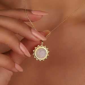 May include: A gold necklace with a round pendant featuring a white, iridescent stone surrounded by a gold, beaded border.
