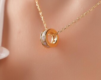 May include: A gold-colored necklace with a double-ring pendant. The pendant features a smaller ring with embedded crystals inside a larger gold ring. The necklace is worn on a person's neck.