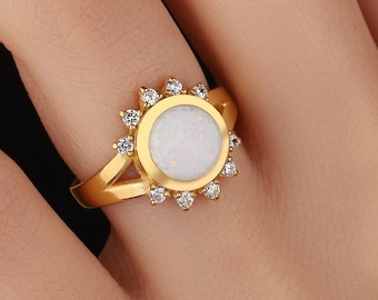 May include: A gold ring with a white opal stone surrounded by small clear stones.