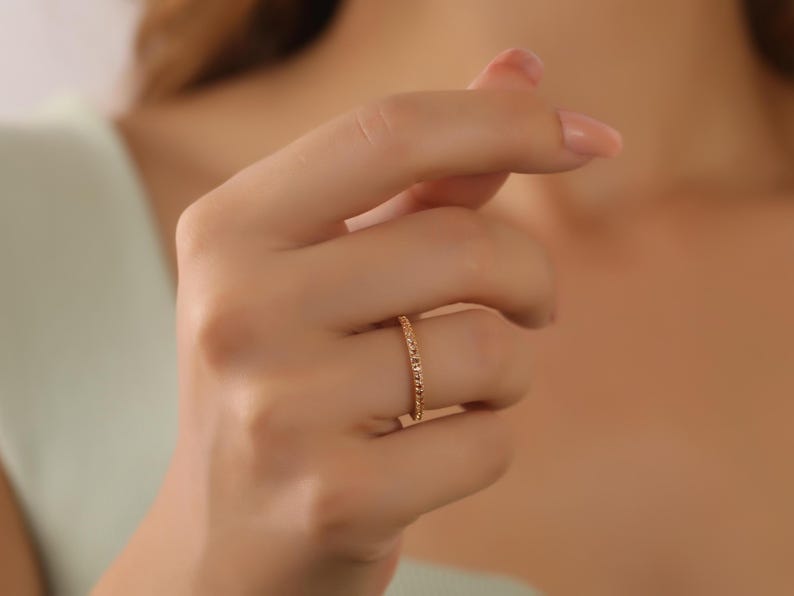 Puede incluir: Un delicado anillo de banda de oro con peque&ntilde;as piedras brillantes engastadas en una l&iacute;nea continua alrededor de la banda.
