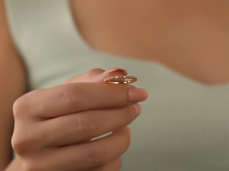 Puede incluir: Un delicado anillo de banda de oro con una fila de peque&ntilde;as piedras preciosas transparentes.