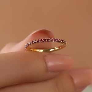 Op de afbeelding: Een dunne gouden ring met een rij kleine, donkerrode edelstenen.