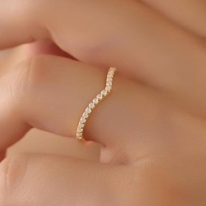 May include: A delicate gold band ring with a wavy line of small, clear stones.