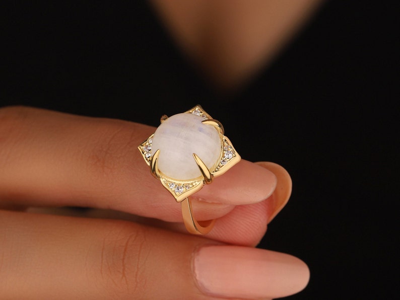 May include: A gold ring with a large, white moonstone set in a geometric design. The ring is accented with small, clear stones.