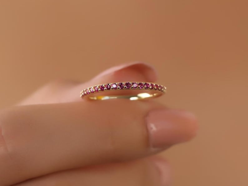 K&ouml;nnte beinhalten: Ein d&uuml;nner Goldring mit einer Reihe kleiner rosafarbener Edelsteine.