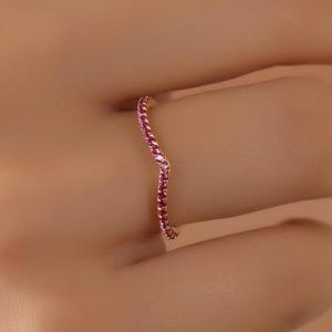 May include: A delicate gold band ring with a chevron design, set with small red gemstones.