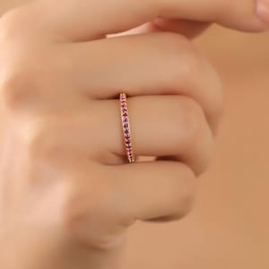 K&ouml;nnte beinhalten: Ein zarter Goldring mit einer Reihe kleiner rosa Edelsteine.