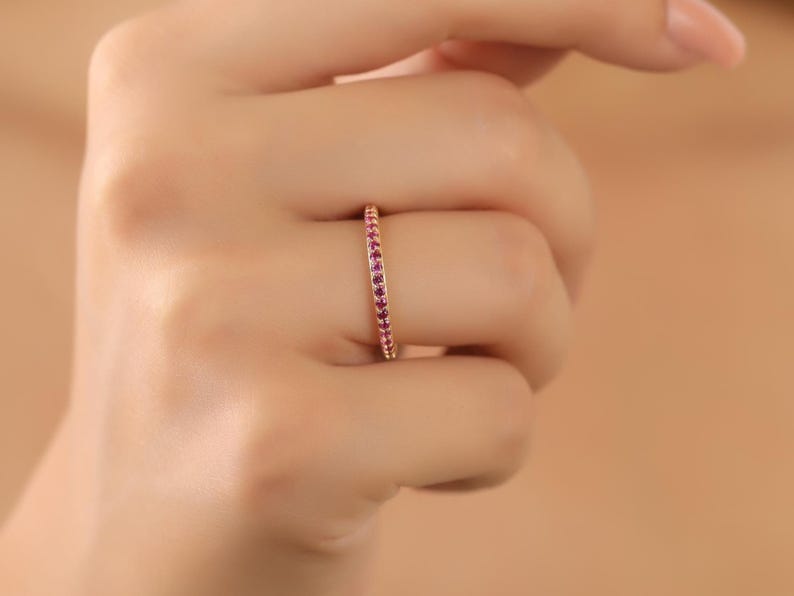 K&ouml;nnte beinhalten: Ein zarter Goldring mit einer Reihe kleiner rosa Edelsteine.