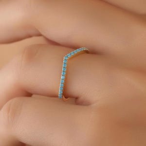 May include: A gold ring with a chevron shape set with small turquoise stones.