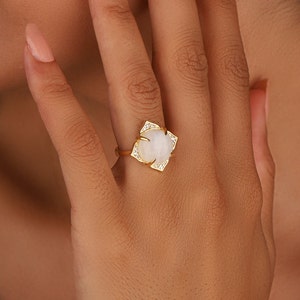 May include: A gold ring with a large white oval gemstone surrounded by smaller clear gemstones.
