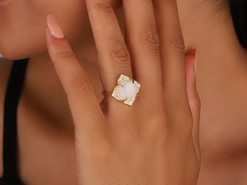 May include: A gold ring with a large white oval gemstone surrounded by smaller clear gemstones.