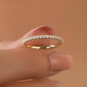 May include: A thin gold band with a row of small, clear diamonds set in a pave setting.