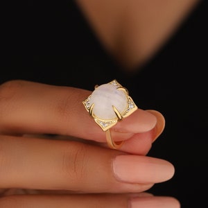 May include: A gold ring with a white moonstone set in a square frame with small clear stones around the edge.