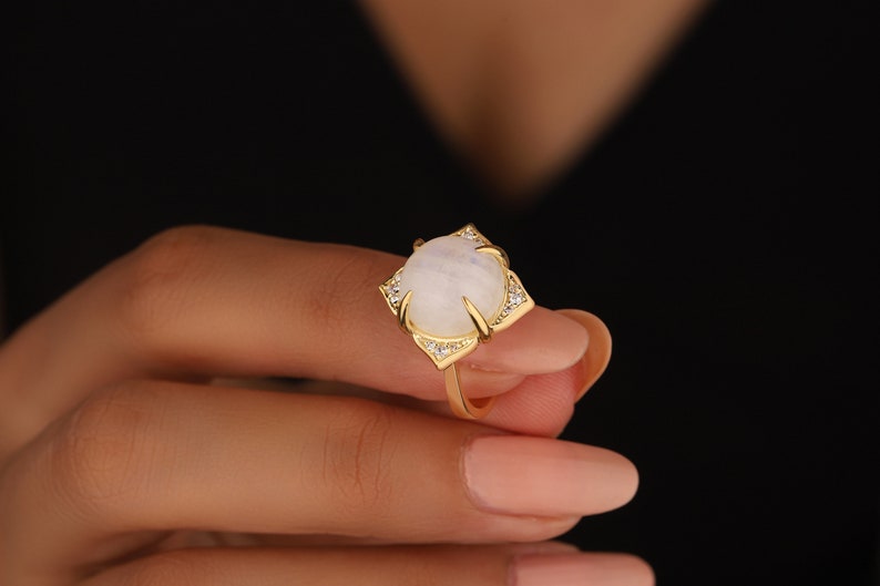 May include: A gold ring with a white moonstone set in a square frame with small clear stones around the edge.