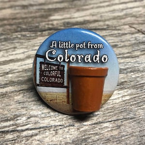 May include: A round button with a blue sky background and a brown terracotta pot. The button says "A little pot from Colorado" and "Welcome to Colorful Colorado".