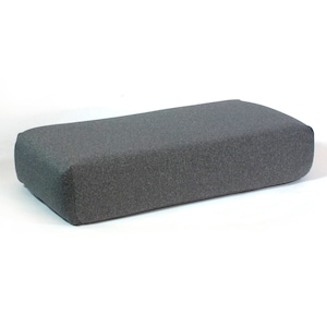 Puede incluir: Un otomano rectangular gris con una cubierta de tela texturizada.