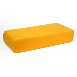 Puede incluir: Un cojín rectangular amarillo con bordes redondeados. El cojín está hecho de una tela suave y mullida.