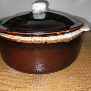 May include: A brown ceramic casserole dish with a lid and a white knob. The dish has a brown glaze with a white rim.
