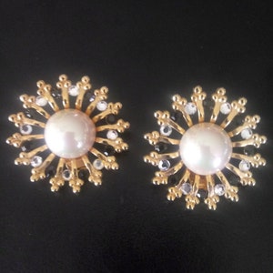 May include: A pair of gold tone earrings with a pearl center and black and white rhinestones arranged in a sunburst pattern.