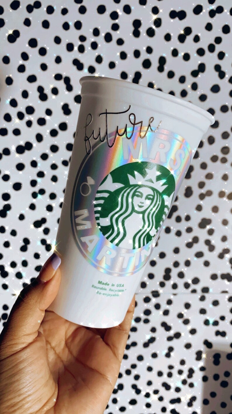 Op de afbeelding: Witte herbruikbare beker met een holografische sticker waarop "future mrs" staat en een groen Starbucks-logo. De sticker heeft een regenboogkleurig, iriserend effect.