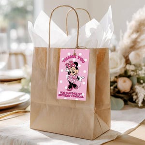 Op de afbeelding: Een bruine papieren cadeauzak met wit vloeipapier en een roze label. Het label toont Minnie Mouse en de woorden "Thank You" en "For Making My Birthday Magical."
