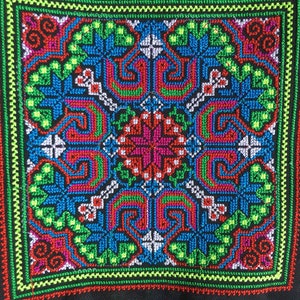 Peut inclure: Un sac en tissu noir avec un motif carré brodé coloré. La broderie présente un motif géométrique avec du fil rouge, vert, bleu et blanc.