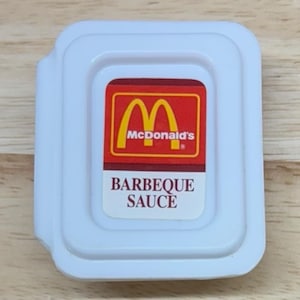 May include: A single-serving packet of McDonald's Barbeque Sauce. The packet is white with a red and yellow logo and the words "BARBEQUE SAUCE" in white text.