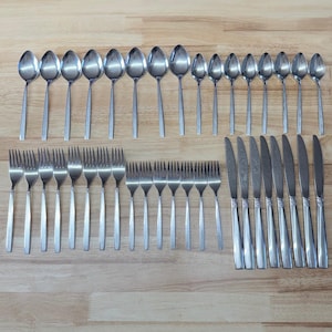 May include: A collection of stainless steel flatware, including spoons, forks, and knives, arranged on a wooden surface. The spoons vary in size, and the knives have decorative handles. The flatware is likely for a formal dining setting.