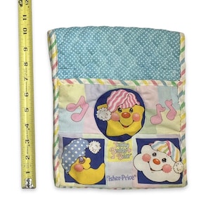 Puede incluir: Un juguete de cuna vintage de Fisher-Price Teddy Beddy Bear. El juguete presenta un diseño acolchado con una parte superior de lunares azules y cuadrados coloridos. Tiene ilustraciones de una estrella, una luna y una nube amarillas con gorros de dormir, con notas musicales. El juguete mide aproximadamente 25 cm de largo.
