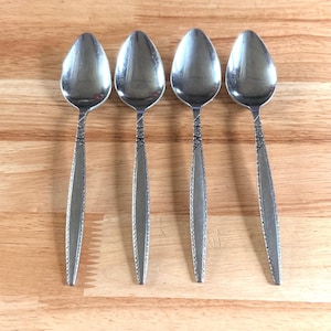 May include: Four stainless steel spoons with a decorative floral pattern on the handles. The spoons are arranged in a row on a wooden surface. The spoons have a classic, elegant design.