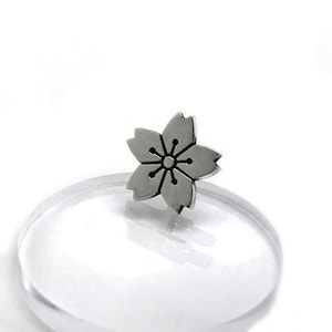 May include: A silver charm in the shape of a cherry blossom flower.