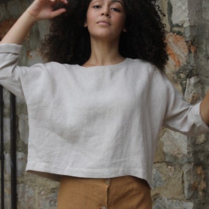 Op de afbeelding: Een vrouw draagt een lichtbeige linnen top met 3/4 mouwen en een bruine linnen rok met knopen.